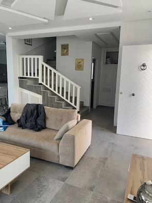 A modern living room with a beige sofa, a wooden coffee table, and a staircase with white railings.