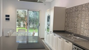 Una cocina moderna con una isla grande, armarios blancos y vistas a un jardín a través de la puerta de vidrio.