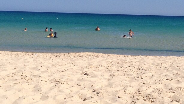 Una playa arenosa con agua azul cristalina y gente nadando y jugando.