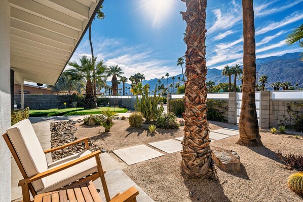 Une terrasse avec une chaise en bois, des palmiers et une vue sur les montagnes.