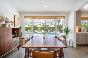 Un vaste espace dédié à la salle à manger, avec une table et des chaises en bois, un meuble encastré et une vue sur une piscine agrémentée de parasols.