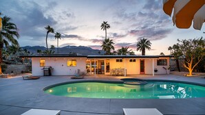 Ein modernes Haus mit Swimmingpool, Terrassenmöbeln und Palmen.