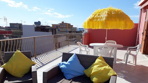 Une terrasse sur le toit, aménagée avec des meubles en osier, un parasol jaune et offrant une vue sur le paysage urbain.