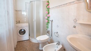 Une salle de bain équipée d’une douche, de toilettes, d’un lavabo et d’un lave-linge.