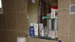 Un baño con un lavamanos blanco, un espejo encima y artículos de tocador en un estante.