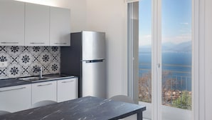 A modern kitchen with a large island, a stainless steel refrigerator, and a view of a lake through a sliding glass door. - Villa Malù - APT Mara Pool and lake view (Torri del Benaco)