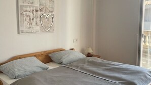 Ein Einzelbett mit Holzrahmen, grauer Bettwäsche und einem Wandbild mit Herzmotiv.
