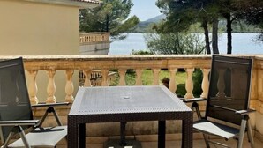 Eine Terrasse im Freien mit Tisch und Stühlen, mit Blick auf ein Gewässer und Bäume.