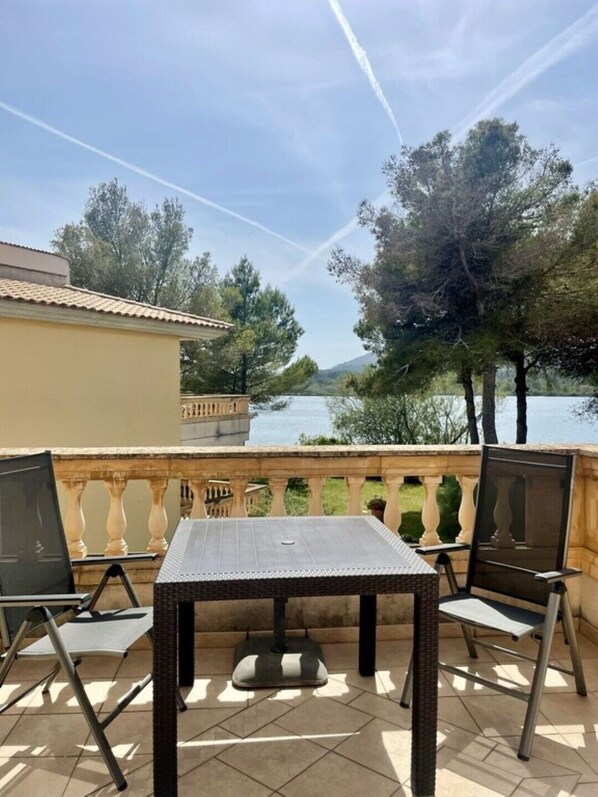 An outdoor patio with a table and chairs, overlooking a body of water and trees.