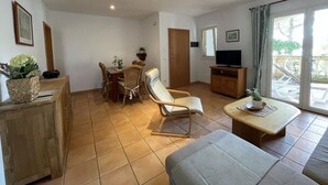 Ein geräumiger Wohnbereich mit Esstisch, Stühlen, einer Couch, einem Fernseher und einer Glastür zum Außenbereich.
