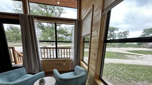 A room with two light blue chairs, a small round table, and a view of a grassy area through large windows.