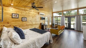 A wooden cabin interior with a bed, sofa, and a ceiling fan.