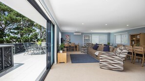 Relax in this spacious living area with a sofa set, coffee table, and bookshelf, leading out to a balcony with a seating area.