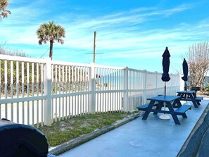 A patio area with white picket fencing, outdoor tables, and umbrellas. - Sandy Feet Retreat  - At Symphony Beach Club! (Ormond Beach)