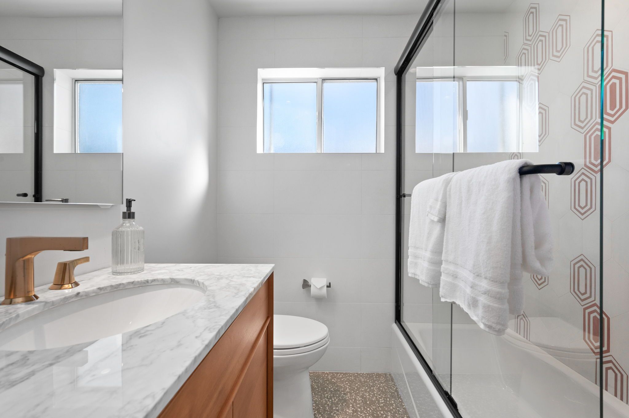 A modern bathroom with a marble sink, a toilet, and a glass-enclosed shower.