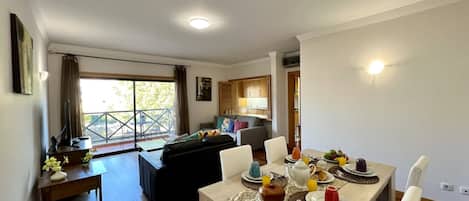 A dining area with a table set for breakfast, a sofa, and a balcony with a view.