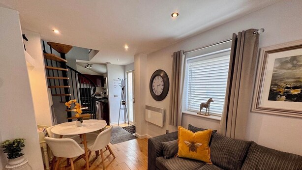 Un salon moderne avec un canapé, une table à manger et des chaises, un escalier et une horloge au mur.
