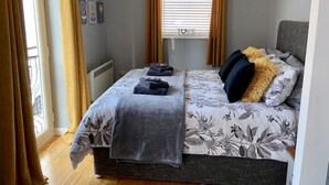 Une chambre à coucher avec un lit, des rideaux, un radiateur et une fenêtre avec des stores.