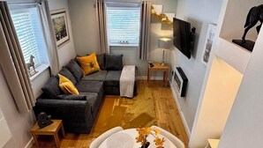 Un espace de vie compact comprenant un canapé, une table à manger avec des chaises et un téléviseur fixé au mur.