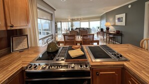 A modern kitchen with a built-in stove, dining area with wooden furniture, and large windows offering a view.
