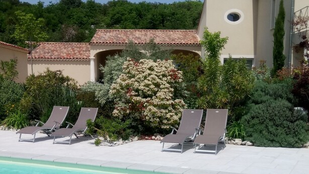Una piscina con agua cristalina, rodeada de sillones de descanso y un jardín con diversas plantas y flores.