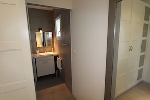 A narrow hallway leading to a bathroom with a sink, mirror, and cabinets. - Le Mas de Molines (Vogue)