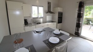 Una cocina compacta con armarios blancos, estufa integrada y comedor para cuatro personas, con mesa, sillas y una ventana con persianas.