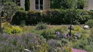 Una casa con techo de tejas, rodeada por un jardín con diversas plantas y flores.
