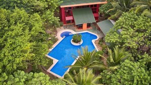 Ein Resort mit Schwimmbad, umgeben von üppiger Vegetation und einem roten Gebäude mit grüner Dachbegrünung.