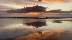 Ein Strand mit ruhigem Wasser, das den Himmel spiegelt.