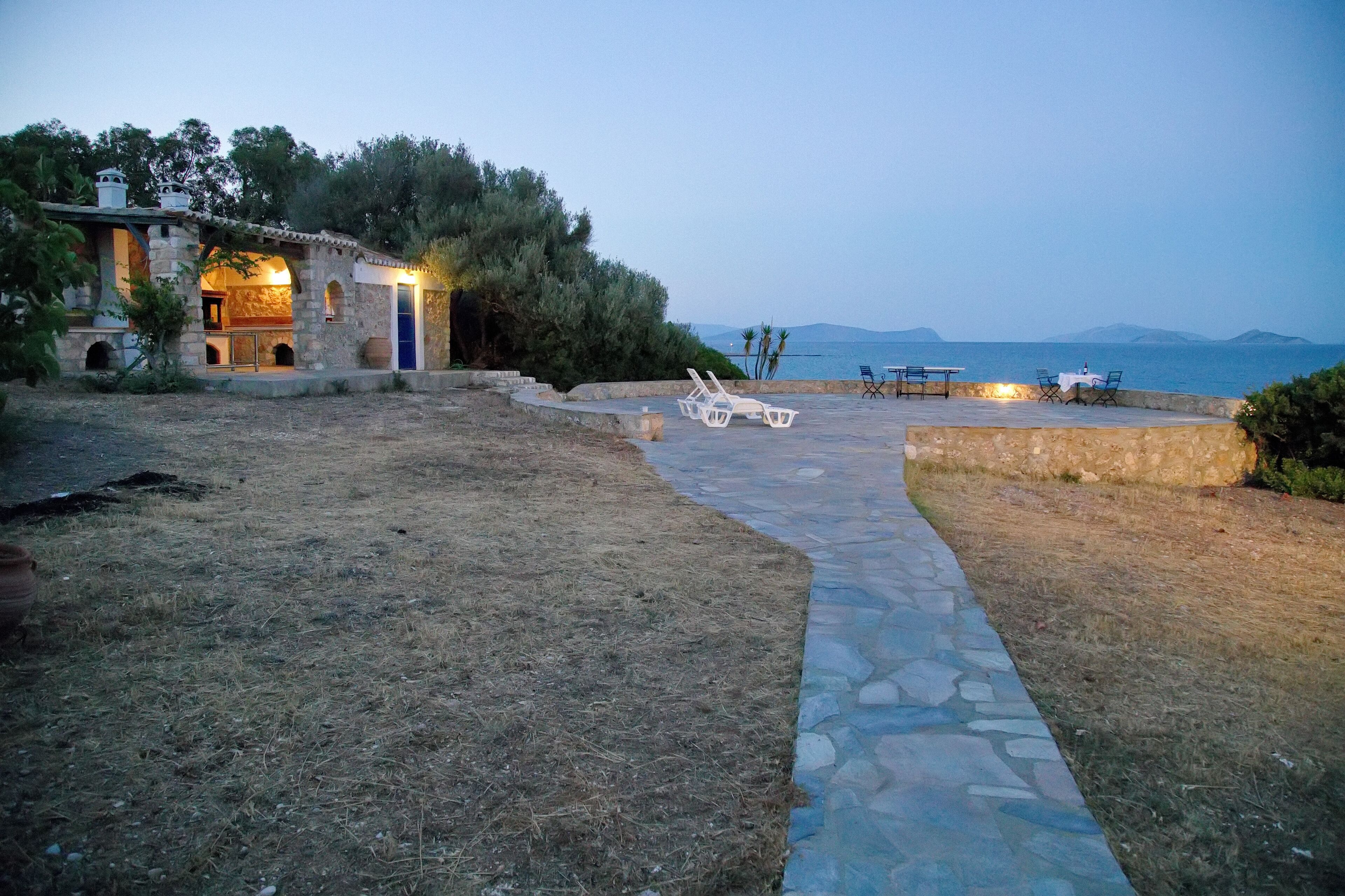 Un chemin de pierre mène à une terrasse dotée de sièges extérieurs et offrant une vue sur la mer.