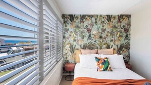 A hotel room with a bed, a view of the sea, and a balcony with railings.
