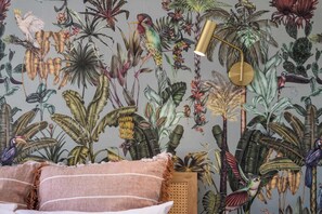 A room with a tropical-themed wallpaper, a bed with striped pillows, and a hanging lamp.