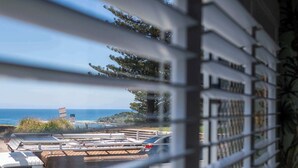 A view through window blinds of a parking area with a beach and ocean in the background.