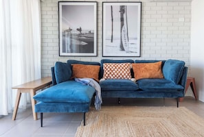 A blue sofa with a matching ottoman, a wooden side table, and a woven rug.