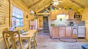 Een gezellig houten cabin interieur met een eethoek, keuken en een trap naar een hoger niveau.