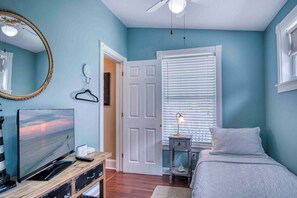 Une chambre à coucher avec un lit, une télévision, une commode, un miroir et une fenêtre avec des stores.