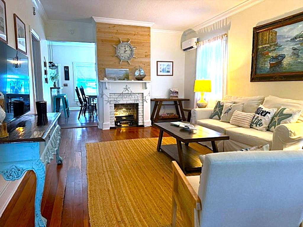 Un salon avec un canapé, une table basse et une cheminée. On aperçoit à l’arrière-plan un coin repas avec des chaises et une table.