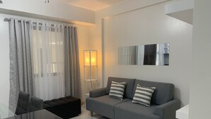 A modern living room with a grey sofa, two striped pillows, a glass coffee table, and a floor lamp. - Modern 2BR Condo at Northpoint, JP Laurel, Davao City (Davao City)