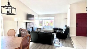 Un salon moderne doté d’une cheminée, d’un téléviseur et d’un coin repas avec une table ronde et des chaises.