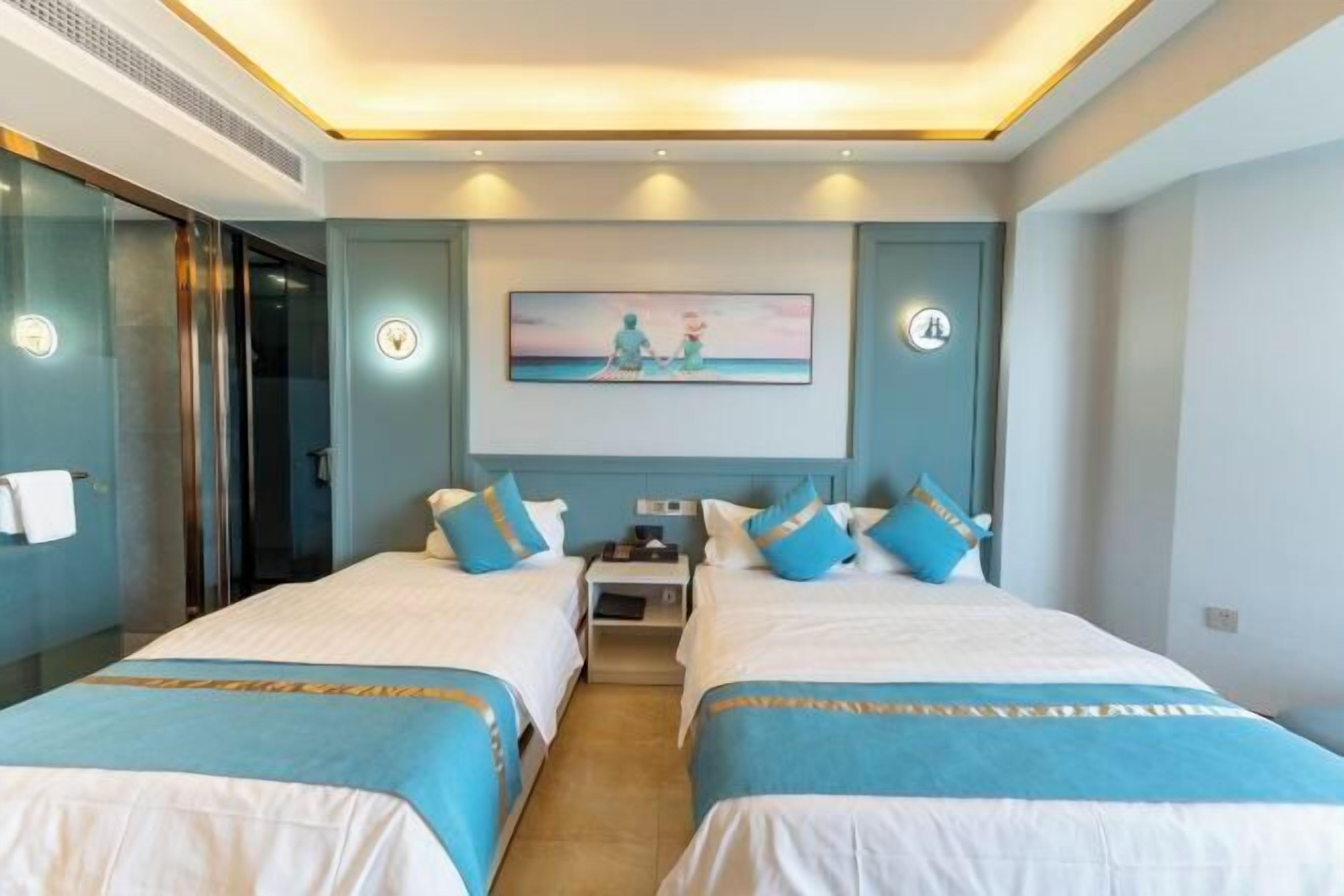 A hotel room with two beds, a painting on the wall, and a small table between them.
