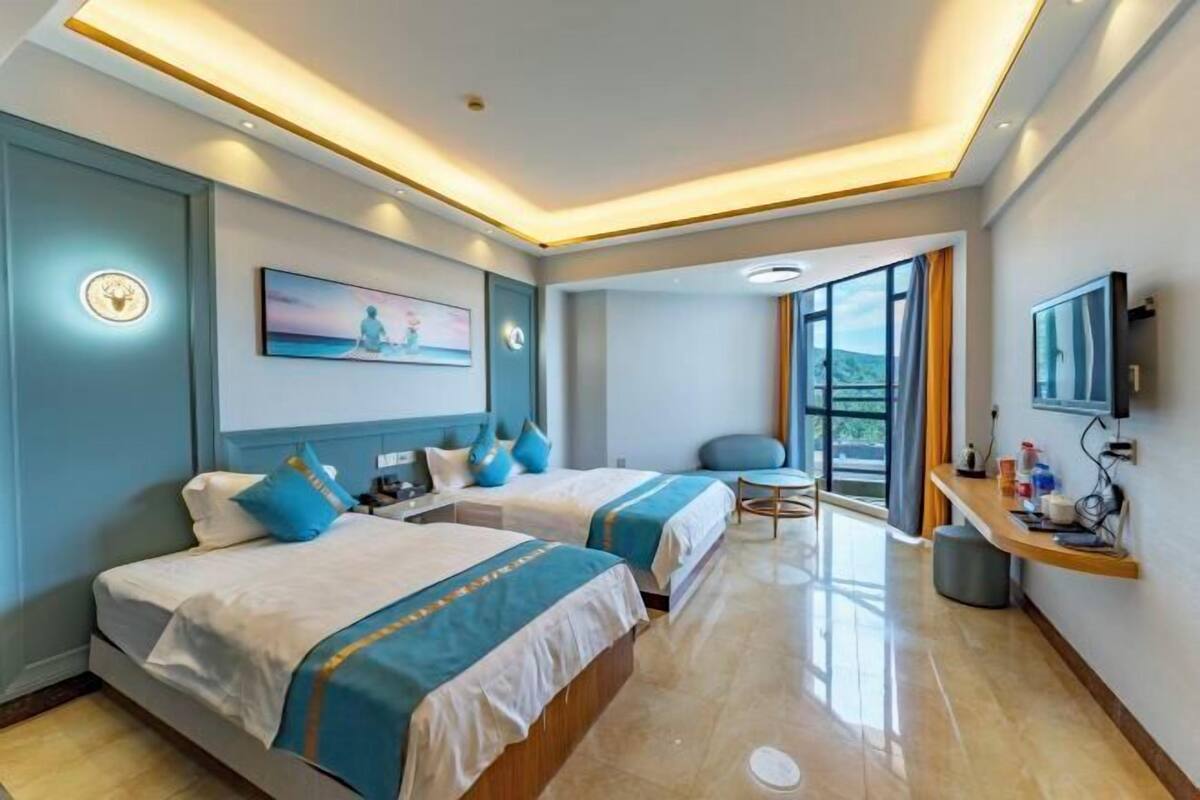A hotel room with two beds, a desk, a chair, a TV, and a large window with a view.