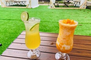 Two drinks on a wooden table outdoors with a green lawn in the background. - Haibin'Ge Hotel (Taishan)