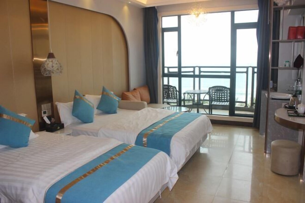 A hotel room with two beds, a balcony with a table and chairs, and a view of the sea.