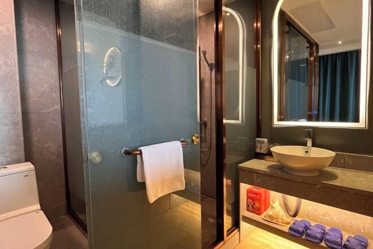 A modern bathroom with a glass-enclosed shower, a white toilet, a sink with a mirror above it, and a towel rack with a white towel.