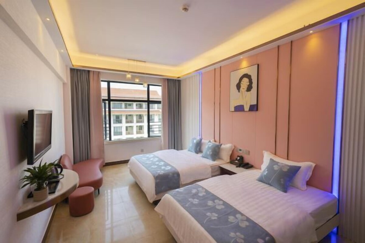 A hotel room with two beds, a TV, a desk with a plant, and a window with curtains.