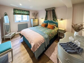 A bedroom with a bed, dresser, vanity, and a window with curtains.