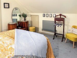 A bedroom with a bed, a dresser, a mirror, a radiator, a chair, and a coat rack.