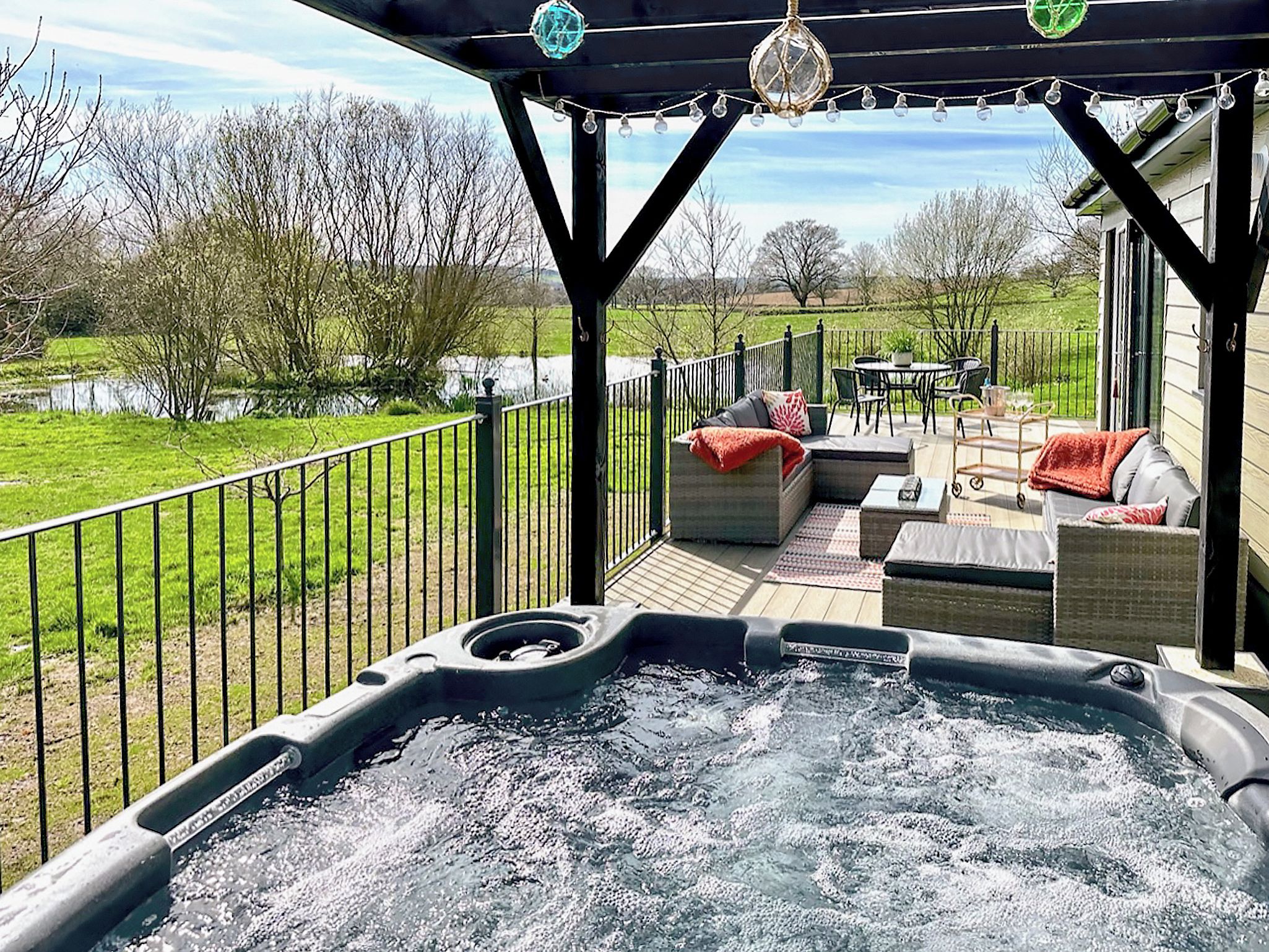 A hot tub on a deck with outdoor furniture and a view of a lake.