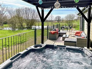 A hot tub on a deck with outdoor furniture and a view of a lake.
